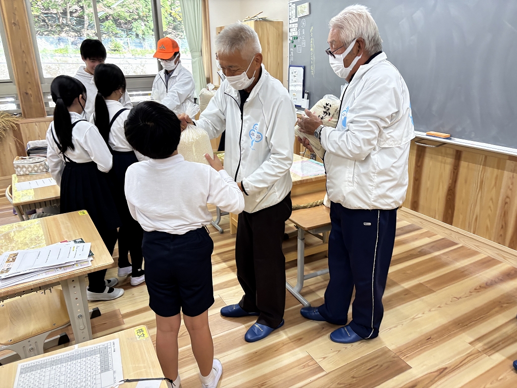 昨年度のおかげ米贈呈式の様子。水土里の会の農家が小学生へお米を渡している。